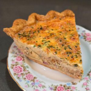 a slice of loaded baked potato quiche with a cheesy creamy quiche filling and bacon bits, potatoes, chives, and caramelized onions