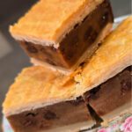 Three slices of Irish Chester Cake stacked on a floral plate, showing layers of golden flaky pastry crust and a dense spiced raisin filling, with a bright green text overlay reading "Irish Gur Cake."