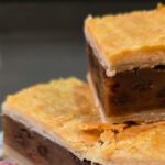 Three slices of Irish Chester Cake stacked on a floral plate, showing layers of golden flaky pastry crust and a dense spiced raisin filling, with a bright green text overlay reading "Irish Chester Cake."