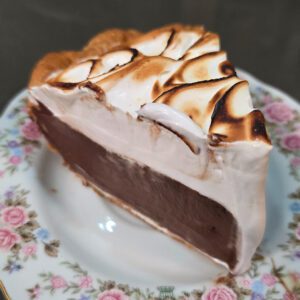a slice of chocolate meringue pie on a floral plate showing homemade chocolate pudding and a toasted meringue topping