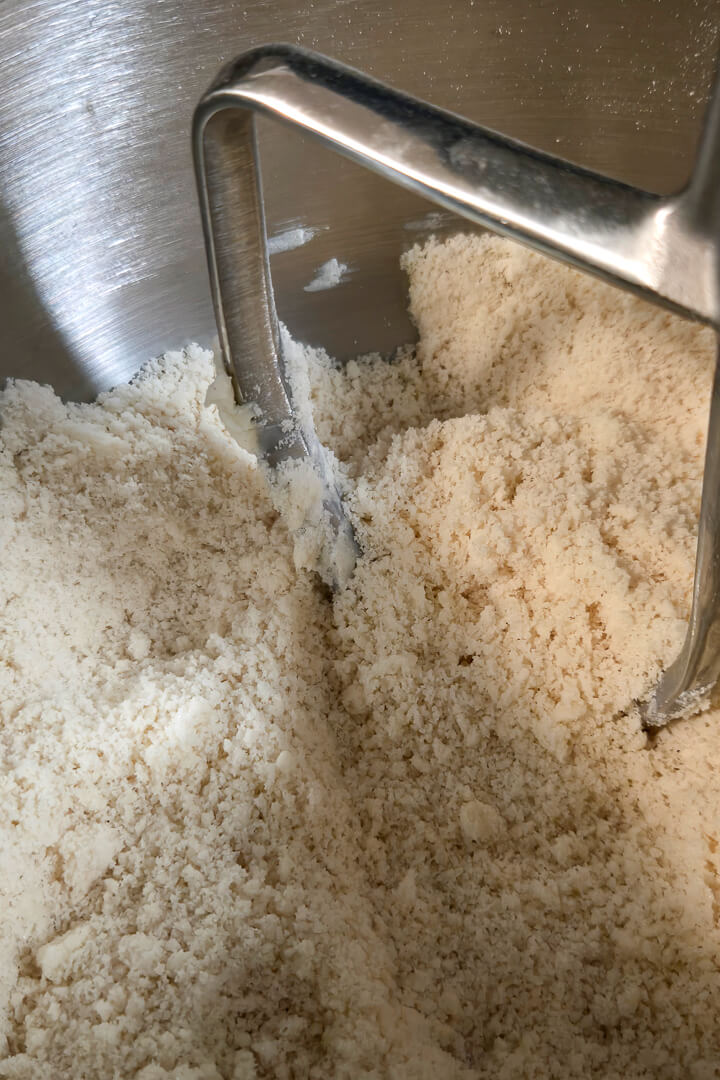 close up photo of softened butter fully cut into flour and sugar in a stand mixer. Part of the process of mixing shortcrust pastry