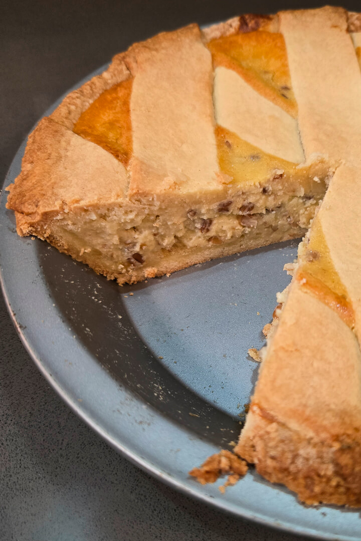 pastiera napoletana with a slice cut out showing the lattice made with pasta frolla on top, and a rich creamy filling studded with wheat berries