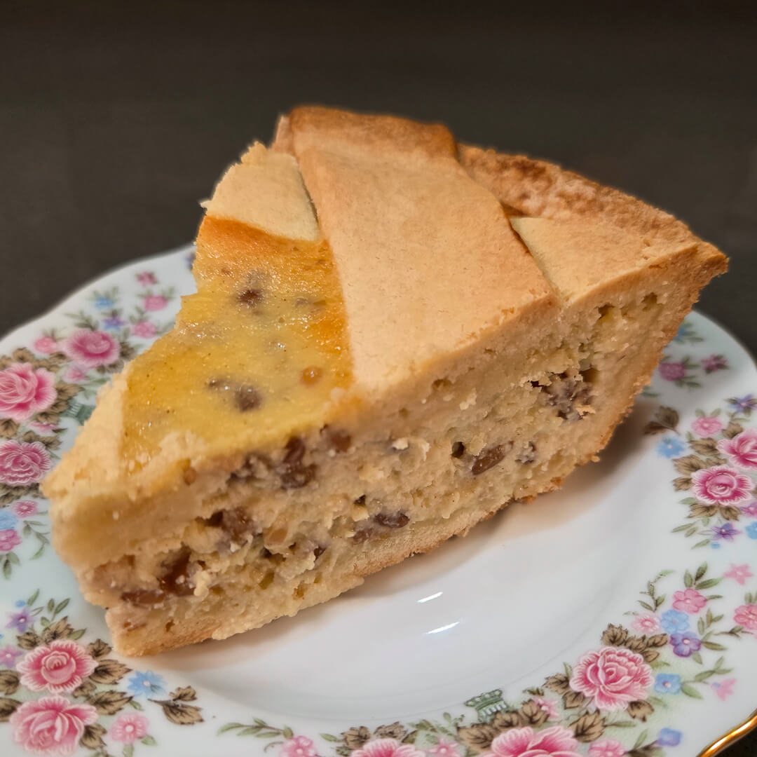 Pastiera Napoletana slice on a floral plate showing golden shortcrust pastry crust and creamy filling of ricotta, wheat berries, and candied orange