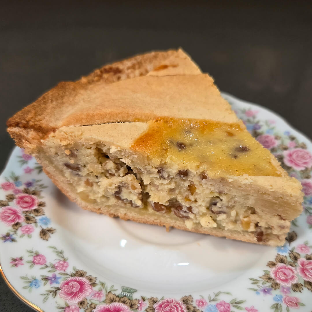 Italian Easter Pie slice on a floral plate showing golden shortcrust pastry crust and creamy filling of ricotta, wheat berries, and candied orange