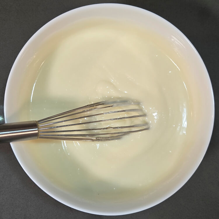 riccota and sugar whisked together in a white bowl with a small metal whisk
