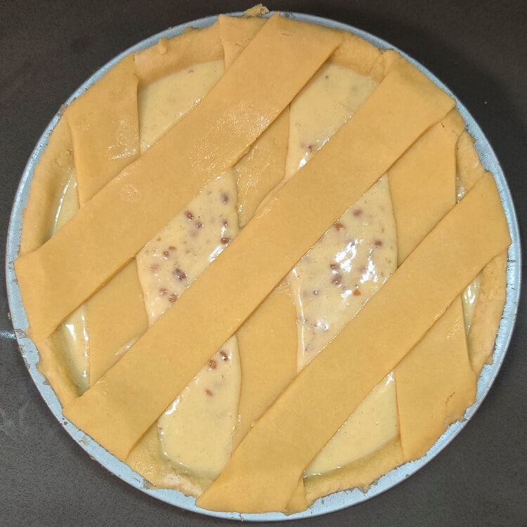 a Pastiera Napoletana before being baked showing unbaked ricotta filling and shortcrust pastry (pasta frolla) laid out in a lattice over top