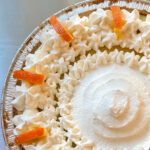 An overhead close-up of a sour orange pie in a graham cracker crust, topped with piped whipped cream rosettes and decorative candied orange peel strips, with text overlay reading "Sour Orange Pie."
