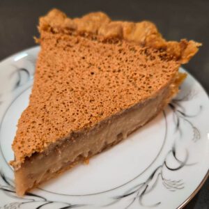 a close up photo of a slice of Bob Andy pie with a crispy golden top and layered look to custard filling on a decorative plate