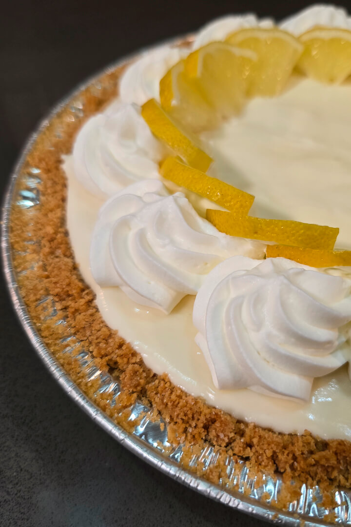 Frozen Lemonade Pie closeup photo in a graham cracker crust topped with swirls of whipped cream and fresh lemon slices