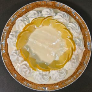 overhead photo of a frozen lemonade pie in a graham cracker crust topped with whipped cream swirls and lemon slices