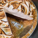 Overhead view of a s'mores pie with a slice cut out, showing layers of graham cracker crust, chocolate ganache, and toasted marshmallow topping. Text overlay reads "A Giant S'more in a Pie! Easy Summer Dessert Recipe." Doggone Baking logo in the bottom right corner.
