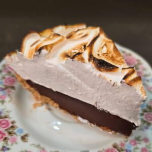 a slice of s'mores pie showing toasted marshmallow topping, chocolate ganache, and graham cracker crust on a floral plate