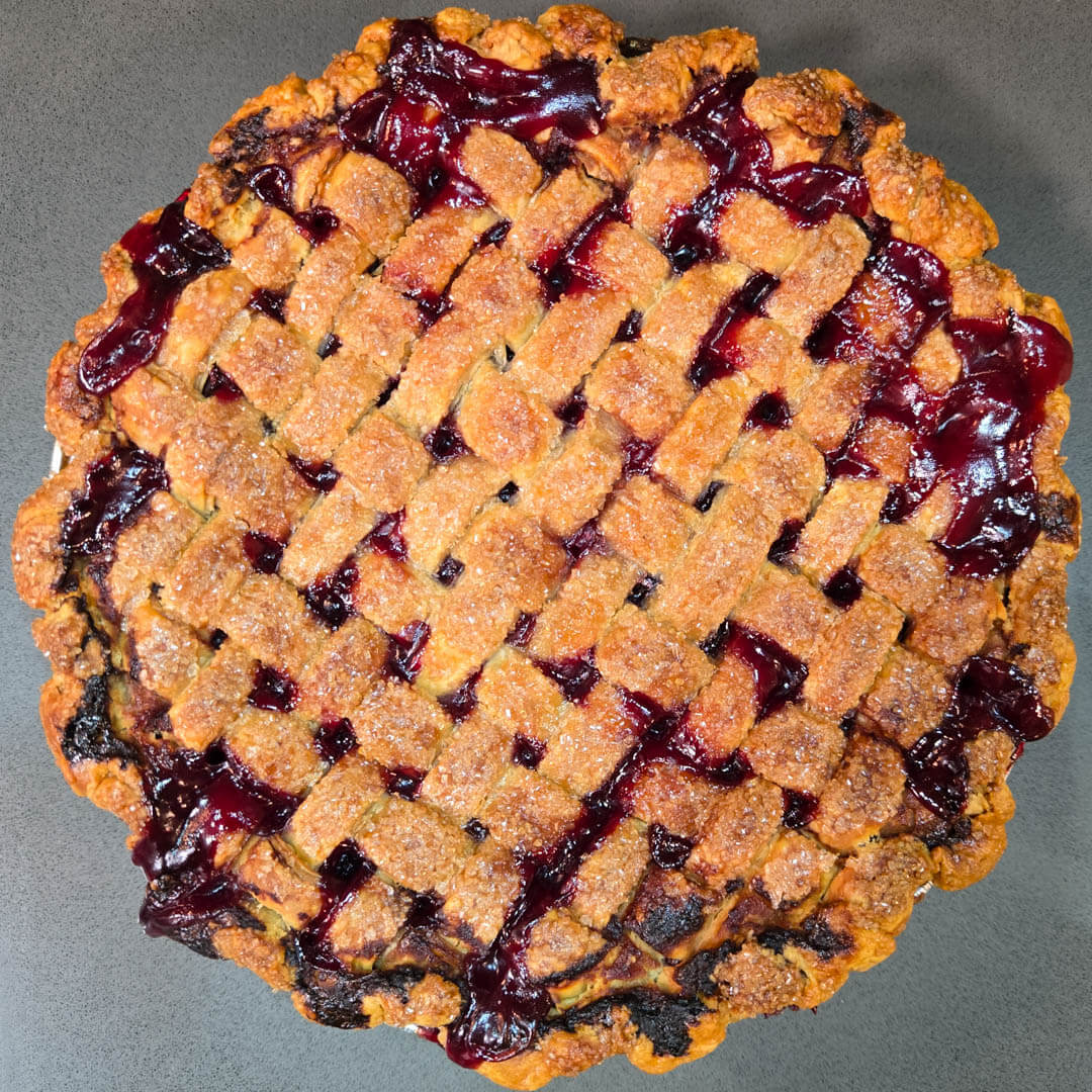overhead photo of a baked cherry pie with a golden skinny lattice top and dark red filling bubbling up