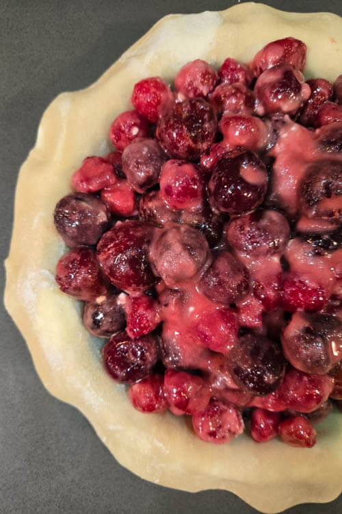 a close up photo of a classic cherry pie before adding the top crust. The unbaked homemade cherry pie filling is inside of a pie tin lined with pie dough.
