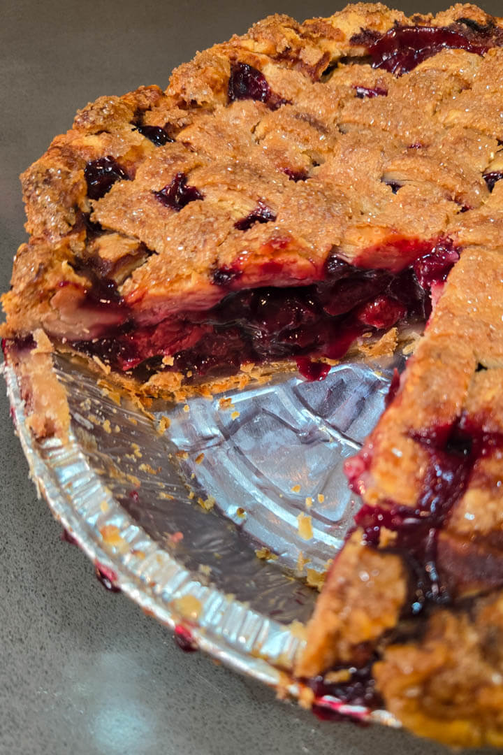 close up photo of a cherry pie with a golden lattice top made with an all-butter pie crust. The filling is juicy and bright red.