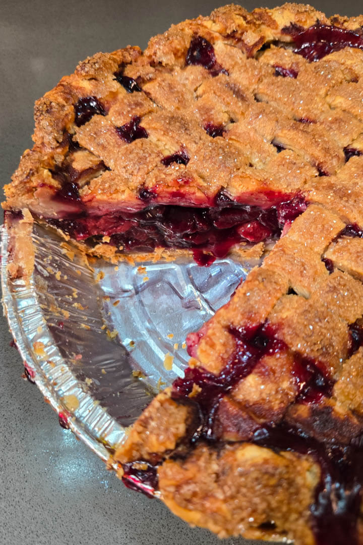 close up photo of a cherry pie with a golden lattice top made with an all-butter pie crust. The filling is juicy and bright red.