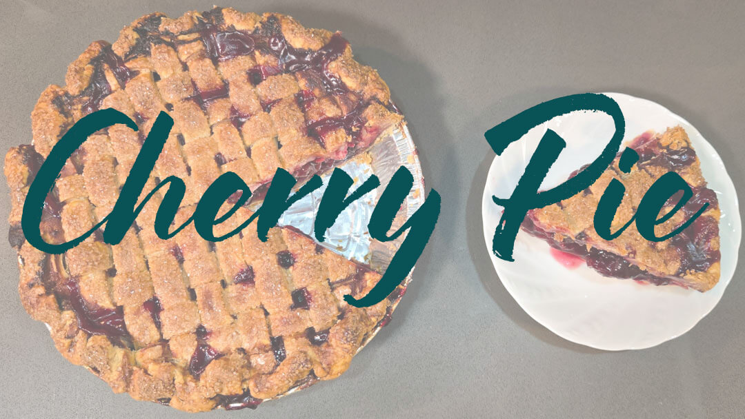 an overhead photo of a cherry pie with a lattice top with a slice cut out and placed next to it on a white plate. Text overlay reads "Cherry Pie"