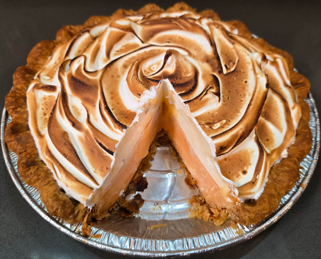 grapefruit meringue pie close up photo with a slice cut out showing a cross section of flaky pie crust, pale pink grapefruit curd, and a toasted fluffy meringue topping