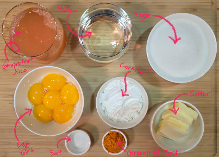 grapefruit curd ingredients laid out on a cutting board with text labels: grapefruit juice, water, sugar, egg yolks, salt, grapefruit zest, cornstarch, butter