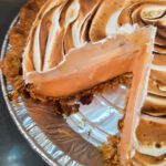 A Pinterest pin for a grapefruit meringue pie recipe. The image shows a close-up angled view of a grapefruit meringue pie with a slice removed, revealing a pale pink grapefruit curd filling topped with a tall elaborately swirled toasted meringue, with the Doggone Baking logo at the bottom. Text overlay reads "Grapefruit Meringue Pie | A Twist on Lemon Meringue Pie."
