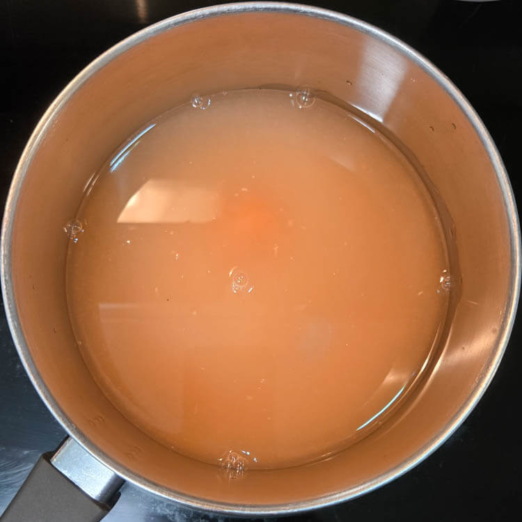 grapefruit juice being heated in a metal pot on a stovetop