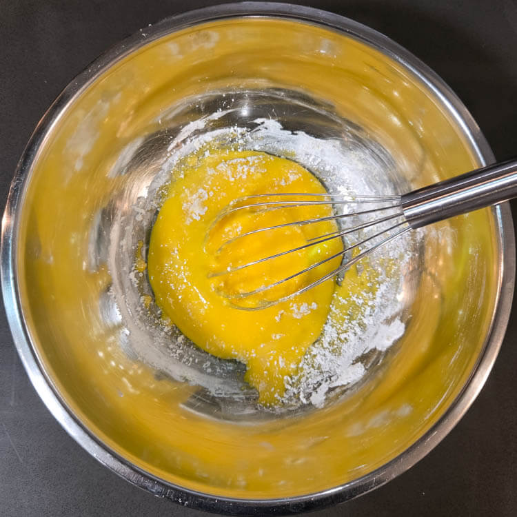 egg yolks whisked with cornstarch in a metal mixing bowl with a metal whisk