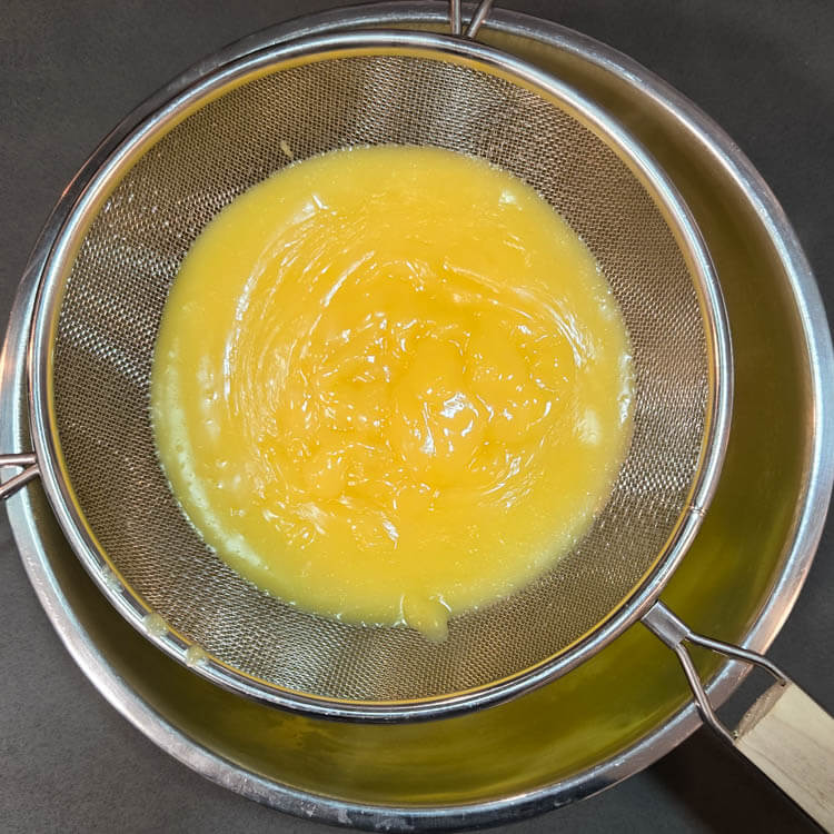 grapefruit curd being strained through a fine mesh strainer to remove lumps
