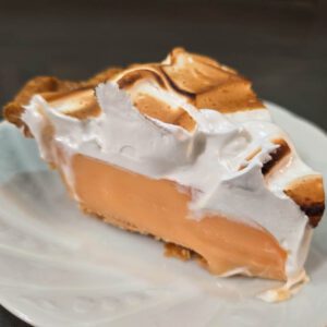 close up photo of a slice of grapefruit meringue pie showing light orange grapefruit curd under a toasted meringue topping on a white plate