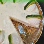 A Pinterest pin for a frozen margarita pie recipe. The image shows a top-down angled view of a frozen margarita pie with a slice removed, revealing a creamy lime filling and a pretzel crumb crust, decorated with piped whipped cream rosettes and lime wedges, with the Doggone Baking logo in the bottom right corner. Text overlay reads "Easy No Bake Dessert Recipe! | Frozen Margarita Pie."