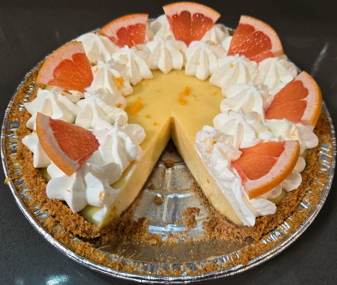 Pink grapefruit pie with a slice cut out with pink grapefruit juice pie filling in a graham cracker crumb pie crust decorated with grapefruit zest, grapefruit slices, and piped whipped cream