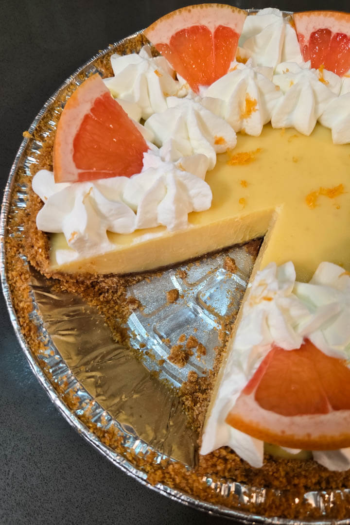 Pink grapefruit pie with a slice cut out. Close up photo with icebox pie filling in a graham cracker crumb pie crust decorated with grapefruit zest, grapefruit slices, and piped whipped cream