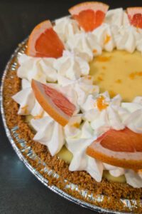 Pink grapefruit pie close up photo with icebox pie filling in a graham cracker crumb pie crust decorated with grapefruit zest, grapefruit slices, and piped whipped cream