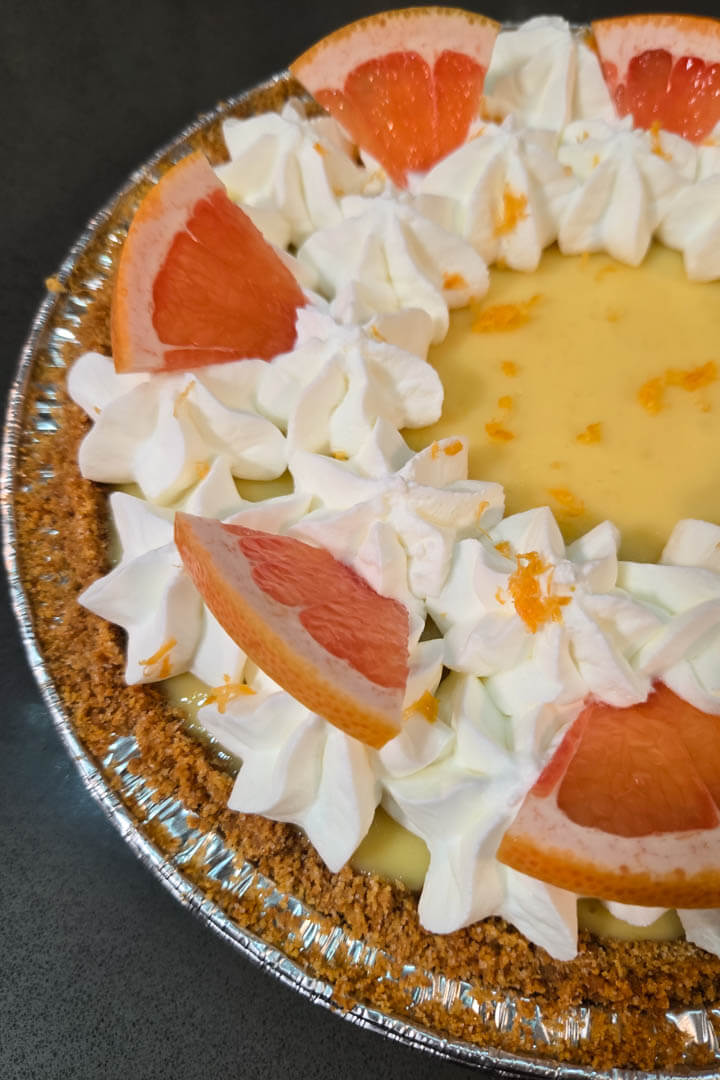 Pink grapefruit pie close up photo with icebox pie filling in a graham cracker crumb pie crust decorated with grapefruit zest, grapefruit slices, and piped whipped cream