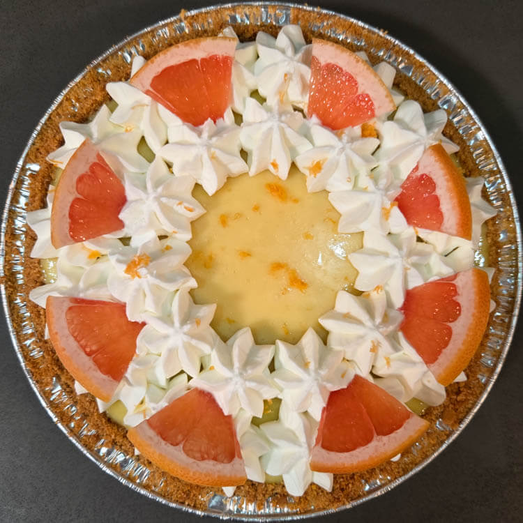 Overhead photo of a Pink grapefruit with pink grapefruit juice pie filling in a graham cracker crust decorated with grapefruit zest, grapefruit slices, and piped whipped cream