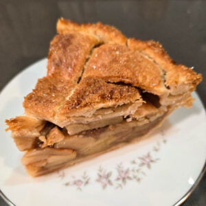 a slice of classic apple pie with a lattice top on a white plate with pink flowers