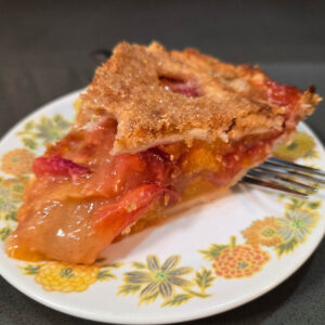 photo of a slice of double-crusted peach pie with a flaky pie crust and homemade peach pie filling on a floral plate with a fork