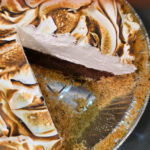 a pinterest pin showing a cross section of a s'mores pie dessert. Graham cracker crust with a chocolate ganache filling topped with a homemade marshmallow fluff recipe. Text overlay reads "S'mores Pie: Homemade Marshmallow Meringue Topping"