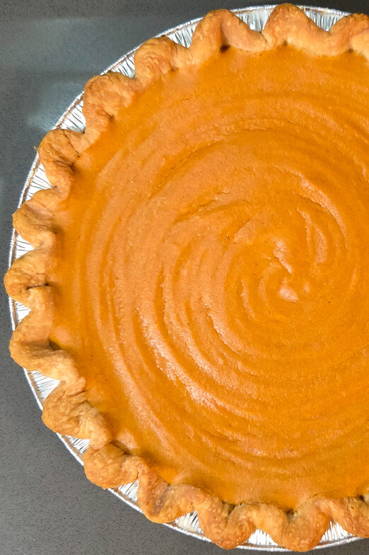 overhead photo of a bright orange brown butter sweet potato pie in an aluminum pie tin with a crimped pie crust