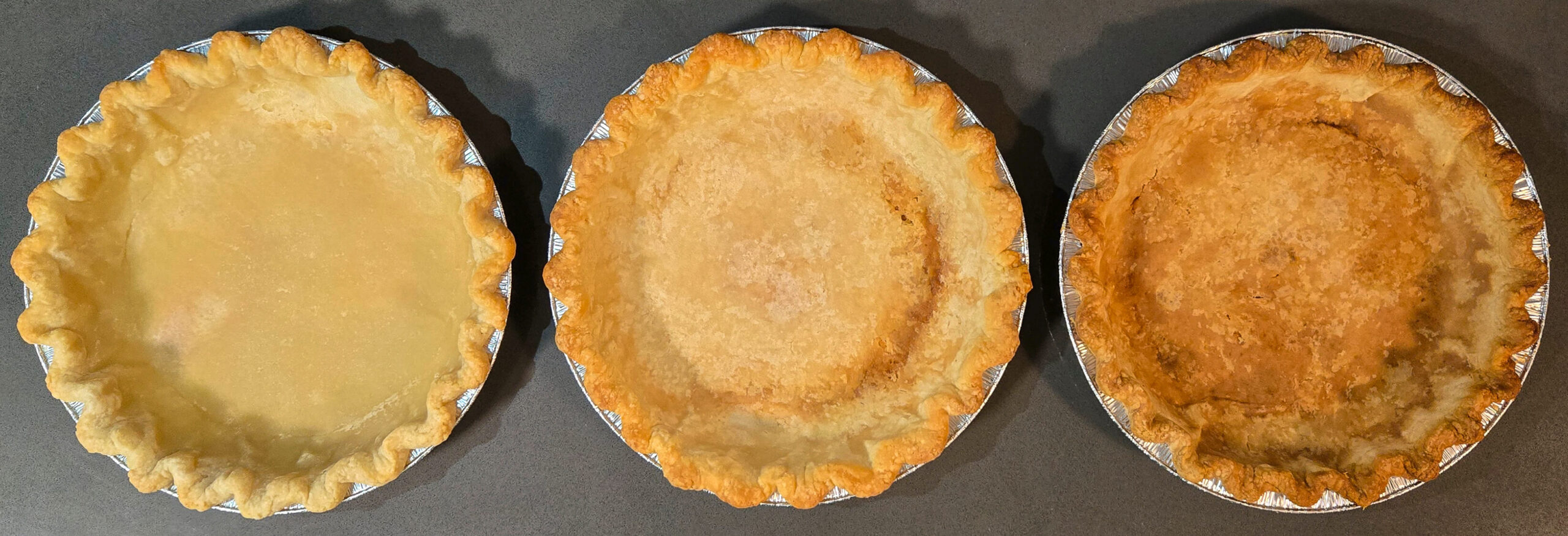 3 blind baked crimped pie shells in a row. A light blind baked pie shell for fruit pies on the left, a dark blind baked pie shell in the middle for custard pies, and a fully baked pie shell on the right for cream pies