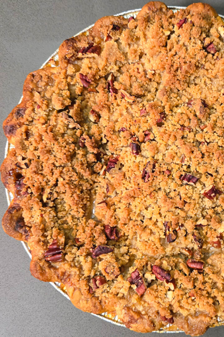 overhead photo of a golden brown caramel apple pie with crimped pie edges topped with a nutty pecan crumb topping