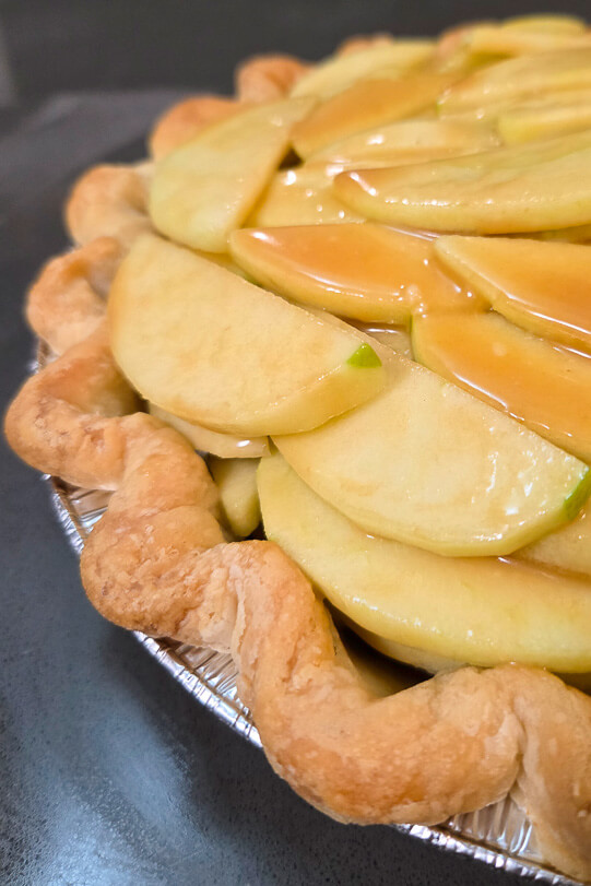 caramel apple pie before being baked with no topping showing apple slices with caramel sauce in a parbaked pie crust