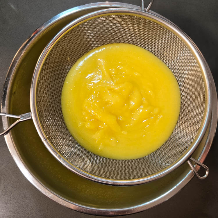 homemade lemon curd being strained through a fine mesh strainer