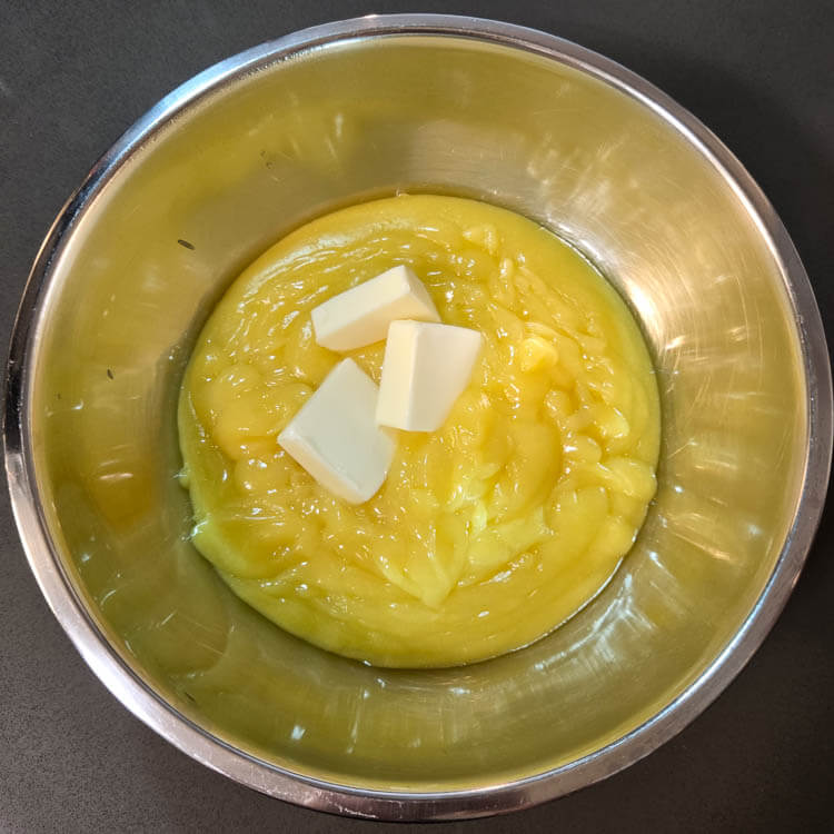 whisking butter into homemade lemon curd in a metal mixing bowl