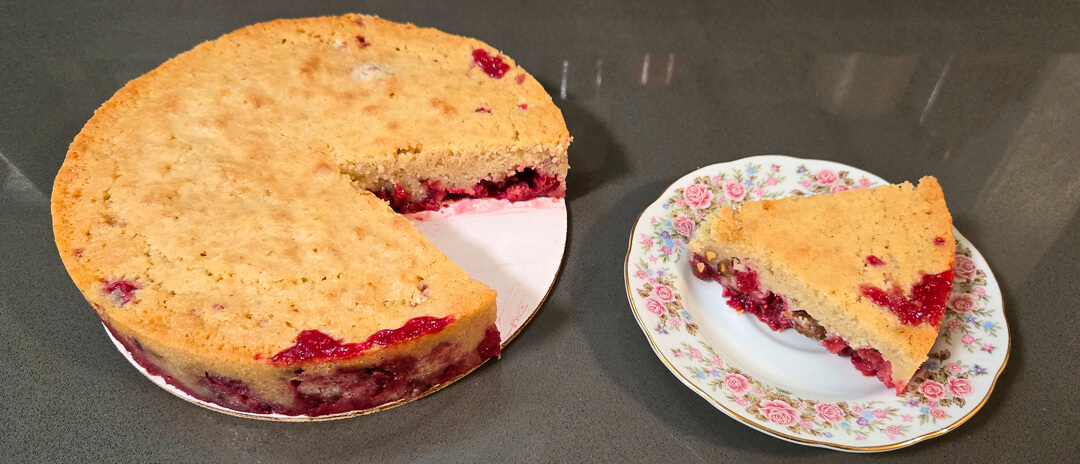 a Nantucket cranberry pie or cranberry upside down cake with a slice cut out and placed next to it on an antique floral plate
