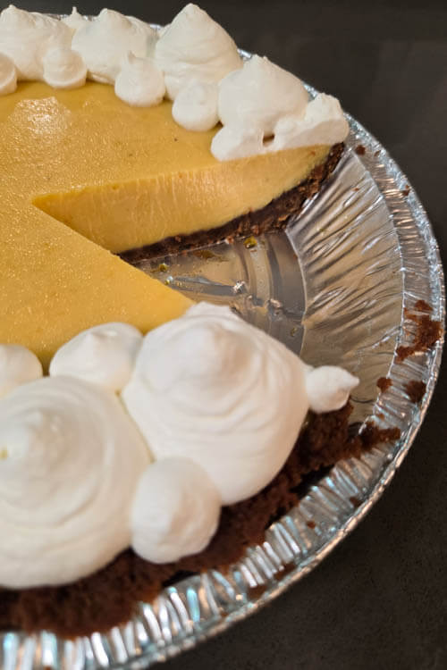 overhead photo of a Brazilian passionfruit pie or Torta de Maracujá in a Biscoff cookie pie crust topped with whipped cream piped in a pattern. A slice is cut out showing the rich passionfruit custard filling