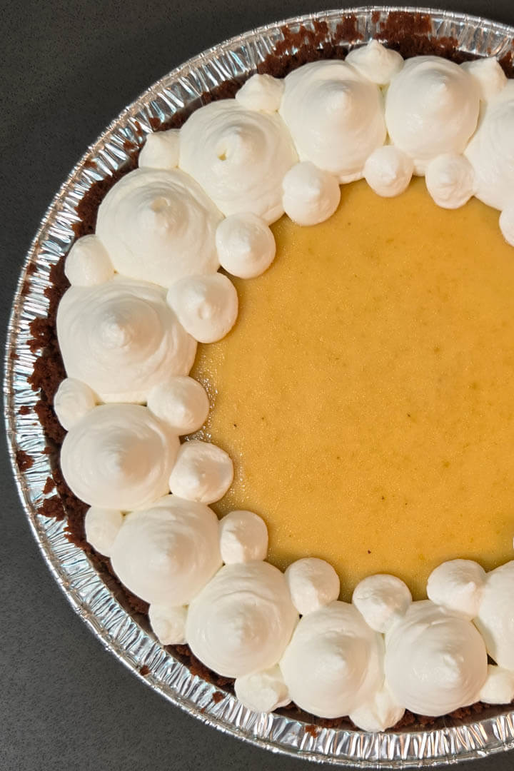 overhead photo of a Brazilian passionfruit pie or Torta de Maracujá in a Biscoff cookie pie crust topped with whipped cream piped in a pattern
