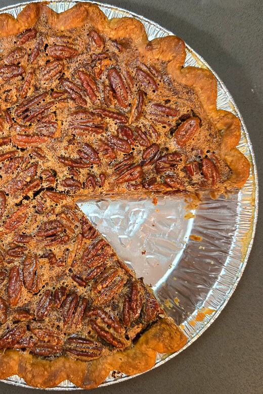 an overhead photo of a Southern pecan pie with golden toasted pecans in a crimped pie crust with a slice removed