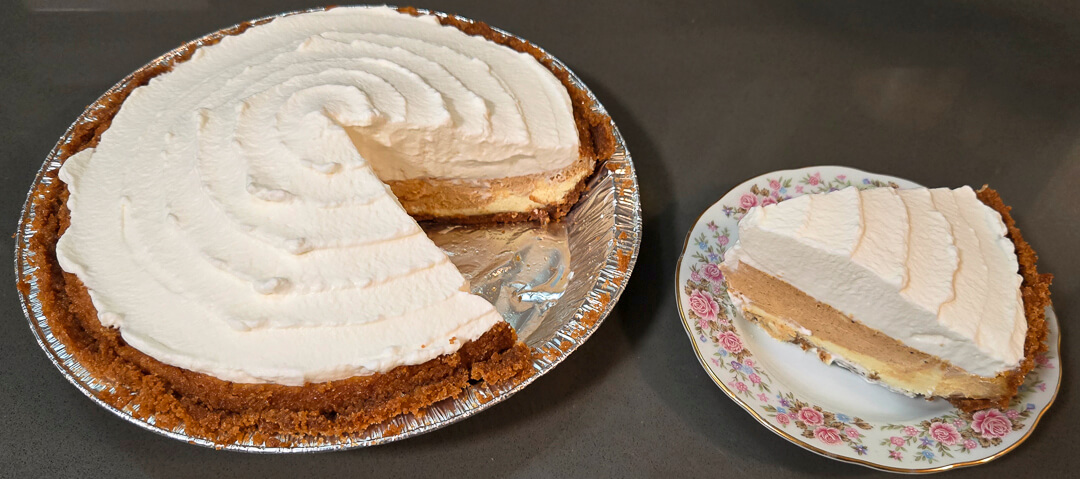 photo of a swirled pumpkin cheesecake in a graham cracker crust topped with whipped cream with a slice cut out and placed on a floral plate next to it