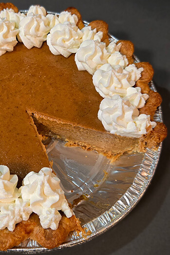 close up photo of a pumpkin pie baked in a crimped pie crust with piped whipped cream and a slice taken out showing a cross section