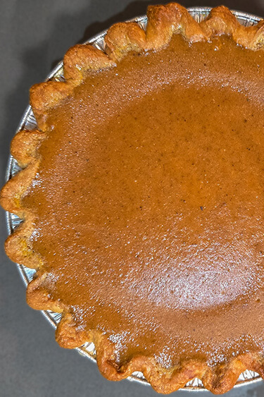 overhead photo of a baked classic pumpkin pie with deep orange spiced pumpkin custard in a crimped pie crust